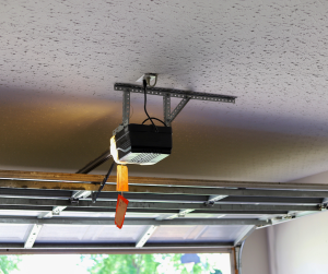 garage door opener mounted to the ceiling in San Diego, with its rail extending towards a partially visible garage door, and a pull-cord release hanging down.